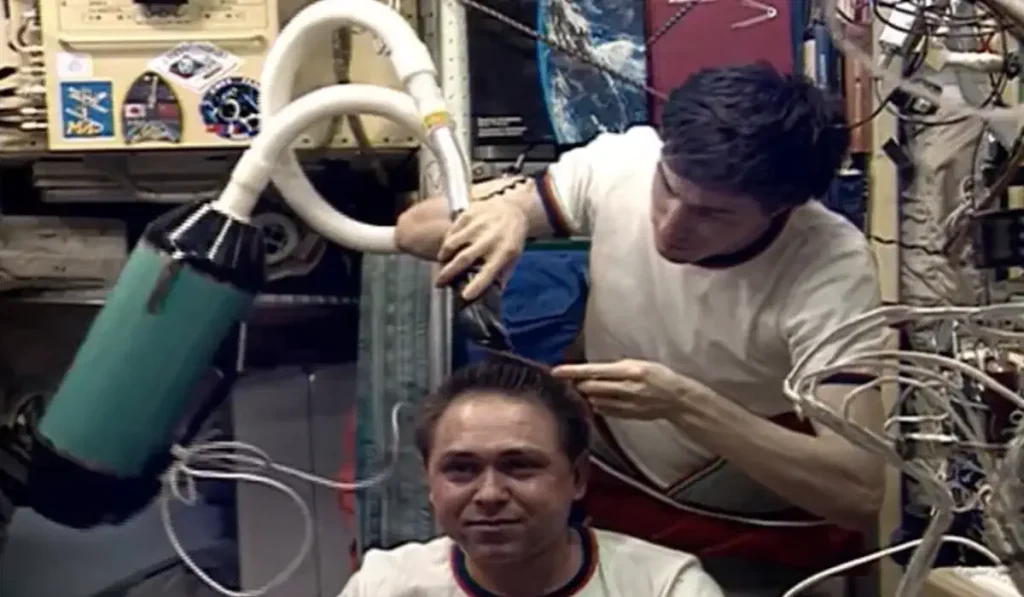 Krikalev cuts the hair of Mir Space Station Commander Alexandr Volkov using a hair clipper with a vacuum attachment